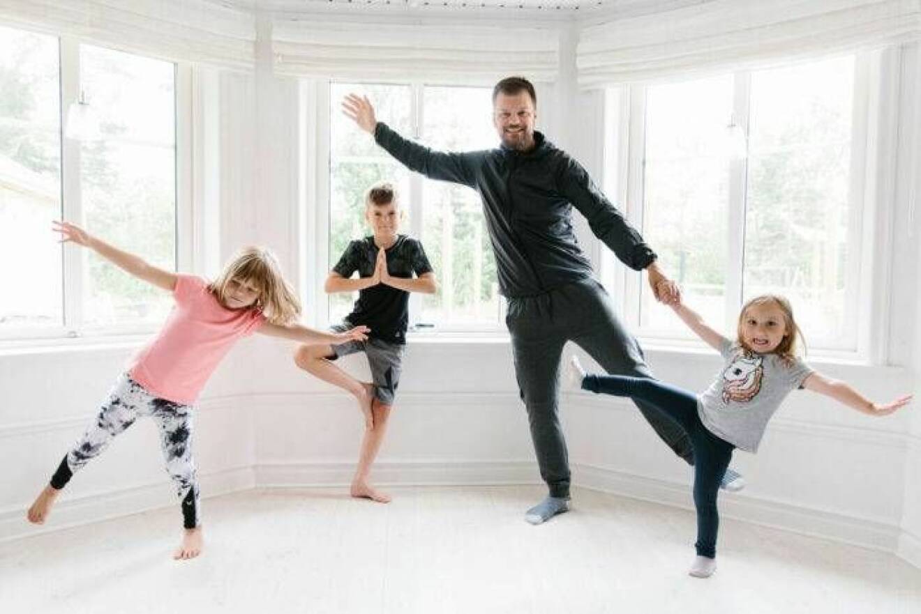 Pappa med tre barn som tränar yoga tillsammans.