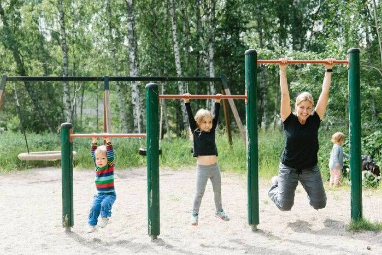 En mamma som tränar i en lekpark tillsammans med sina två barn.