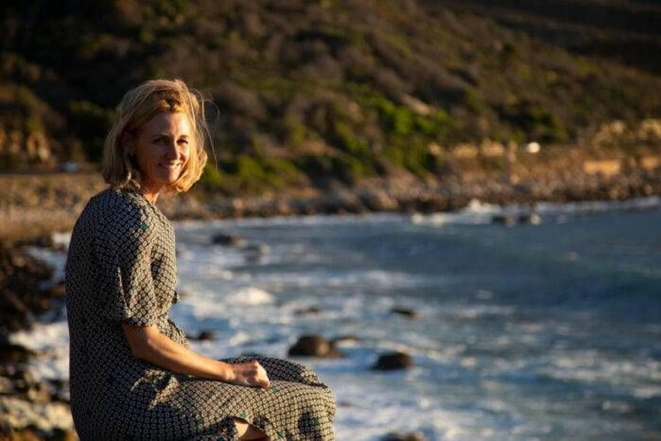 Marie Sammeli sitter vid vattnet i Sydafrika med ett berg i bakgrunden. 