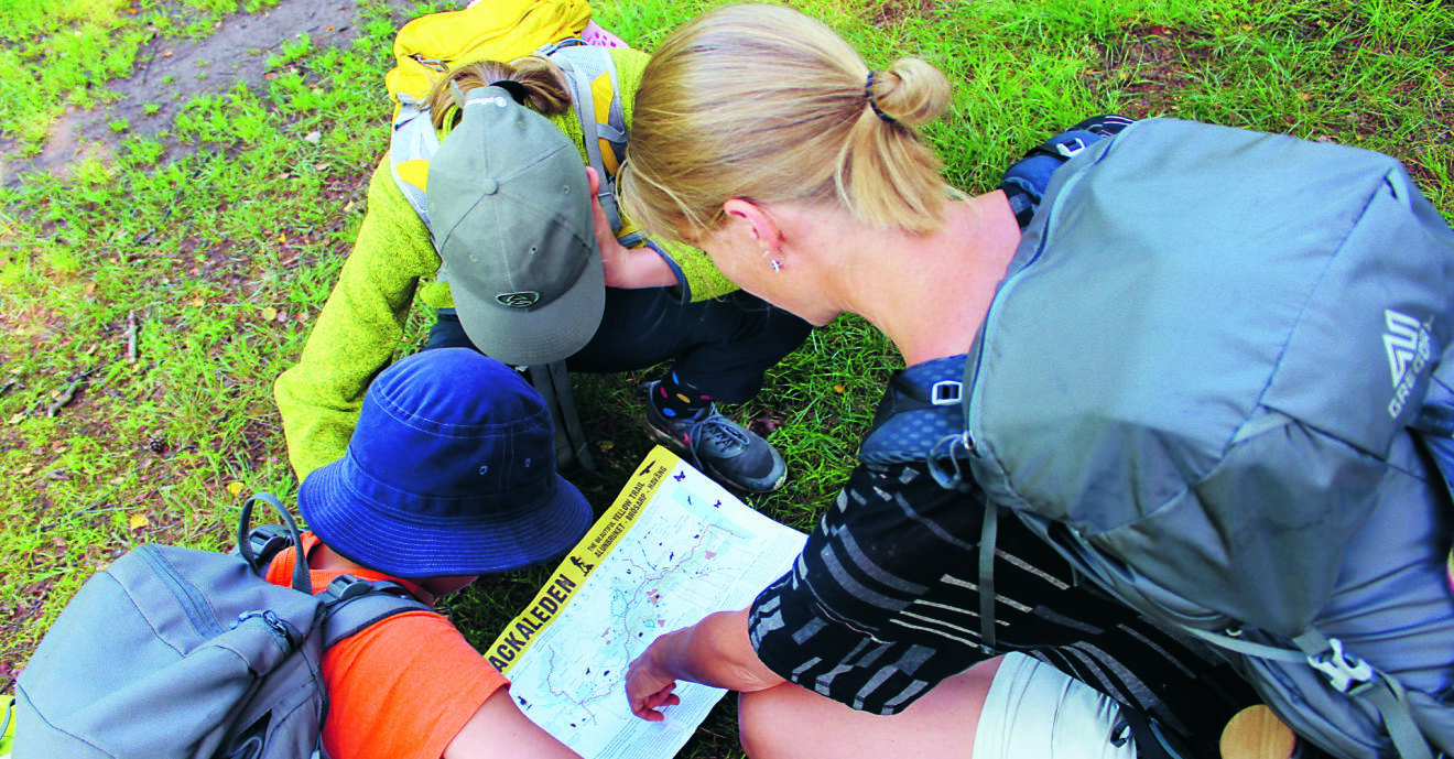 En kvinna och två barn läser en karta under en vandringstur.