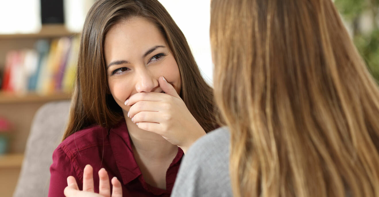 En ung kvinna döljer sina tänder i ett samtal med en vän.