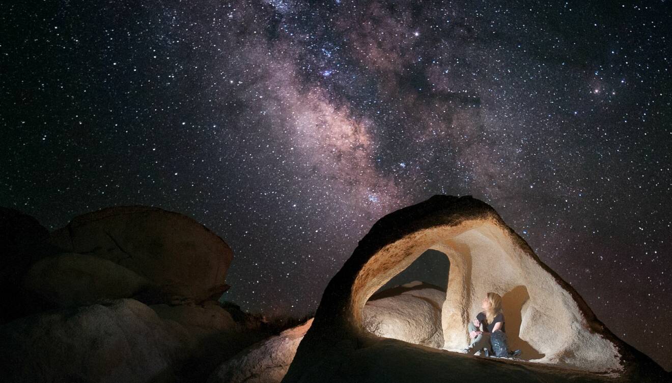 En kvinna i en grotta som tittar på stjärnspäckad himmel.