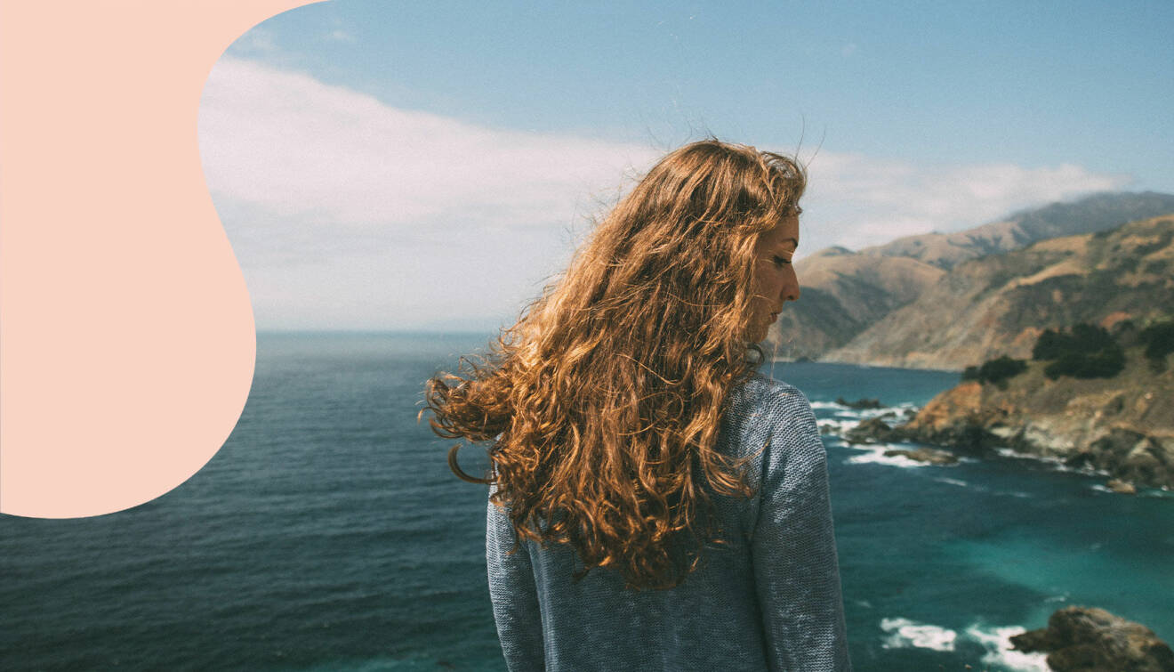 En kvinna med stort hår ser ut över havet.