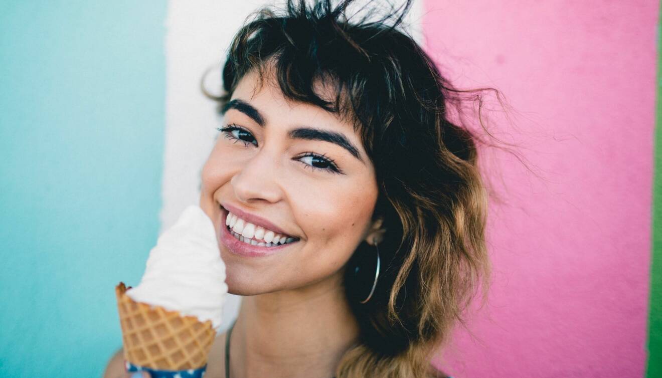 Leende kvinna äter glass framför färgglad bakgrund.