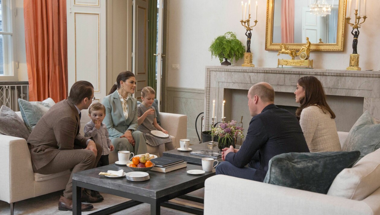 Hemmet i Haga är modernt och går i vit och grå färgskala. Här besöks kronprinsessfamiljen av ”kollegorna” William och Kate 2018. Hela familjen i en beige soffa och Kate och William mitt emot i en annan soffa. På bordet tända ljus, frukt och blommor.