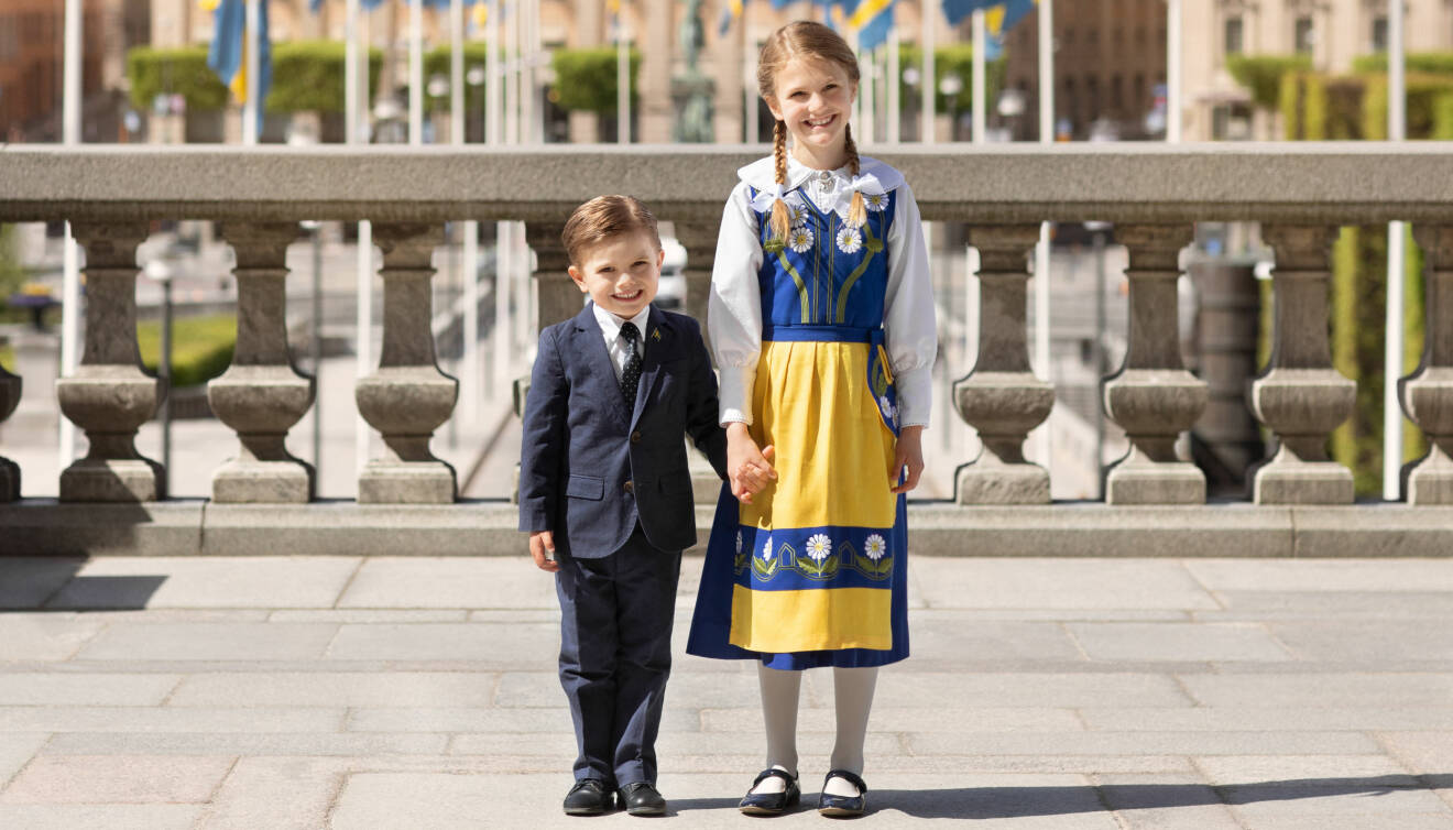 Prinsessan Estelle och prins Oscar håller varandra i handen iklädda Sverigedräkt och kostym på nationaldagen den 6 juni 2020.