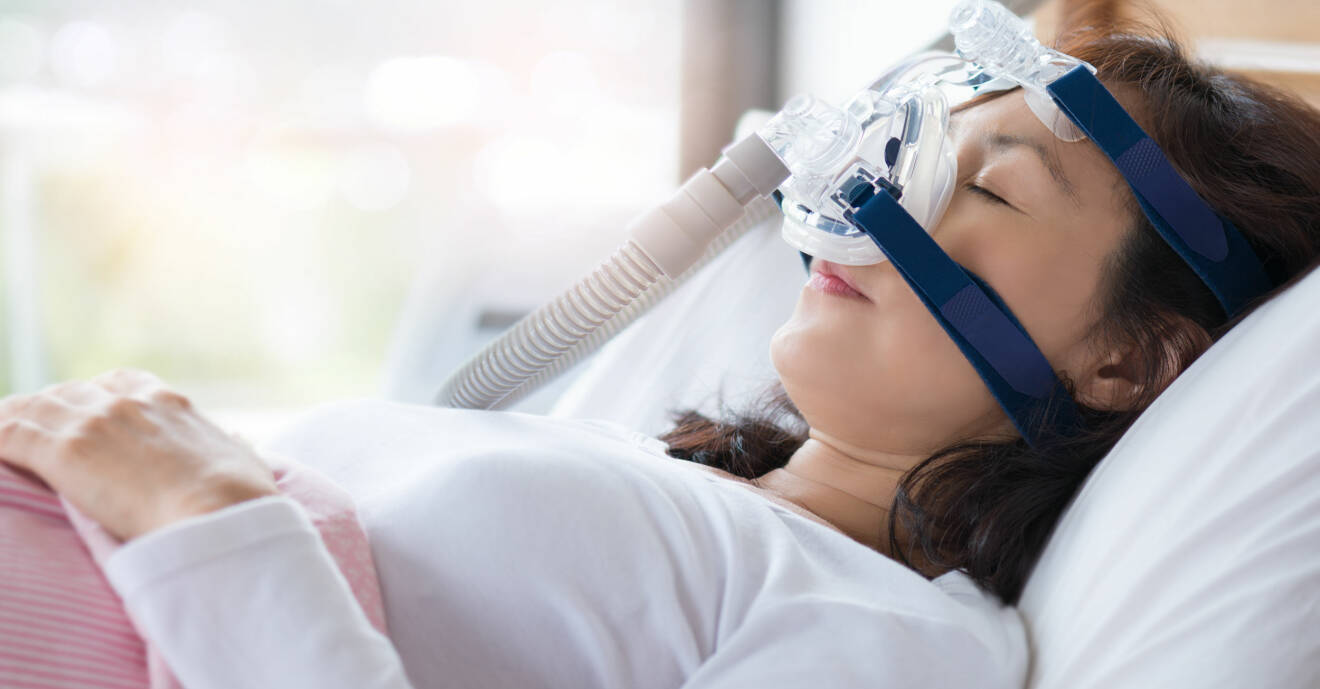 En kvinna sover i sin säng med CPAP-apparat.