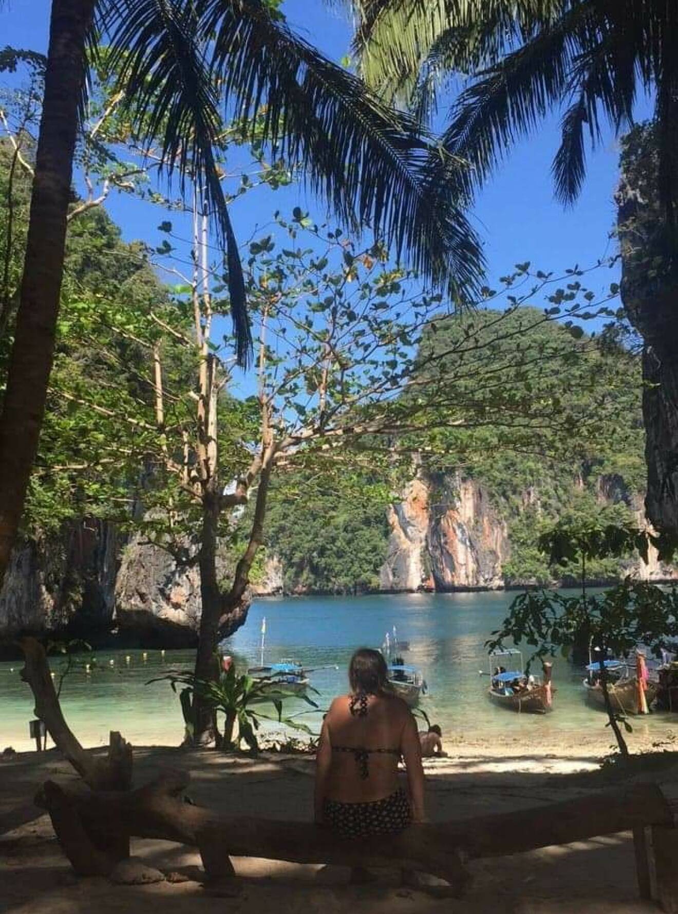 Susanne Bohlin på en Thailändsk strand med palmer, blå himmel och klippor.