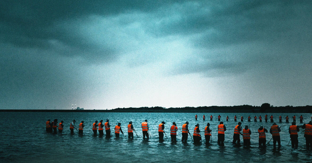 En scen ur tv-serien Utredningen, där en mängd människor med orange västar söker efter något i vattnet.