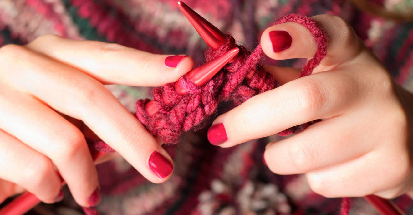Bild på händer med rött nagellack som stickar med rött garn.