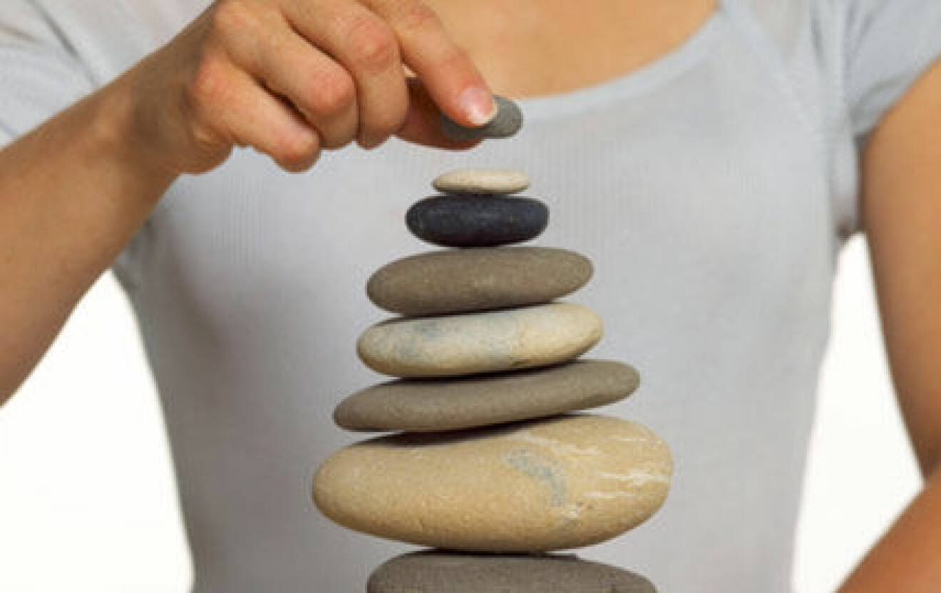 Bild på en hög med stenar som balanserar på varandra. Bakom syns en person i ljus grå tröja och en hand som lägger en liten sten överst i högen.