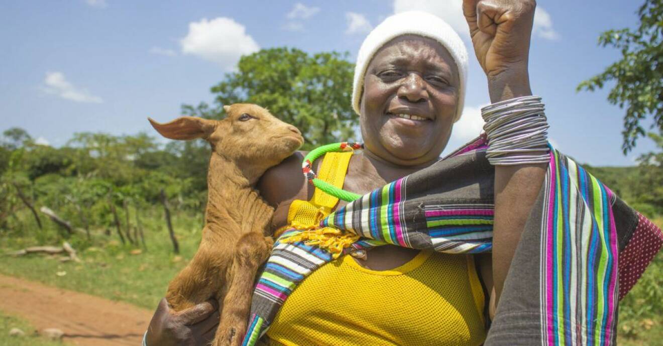 En kvinna i ett afrikanskt land som håller en get under armen.
