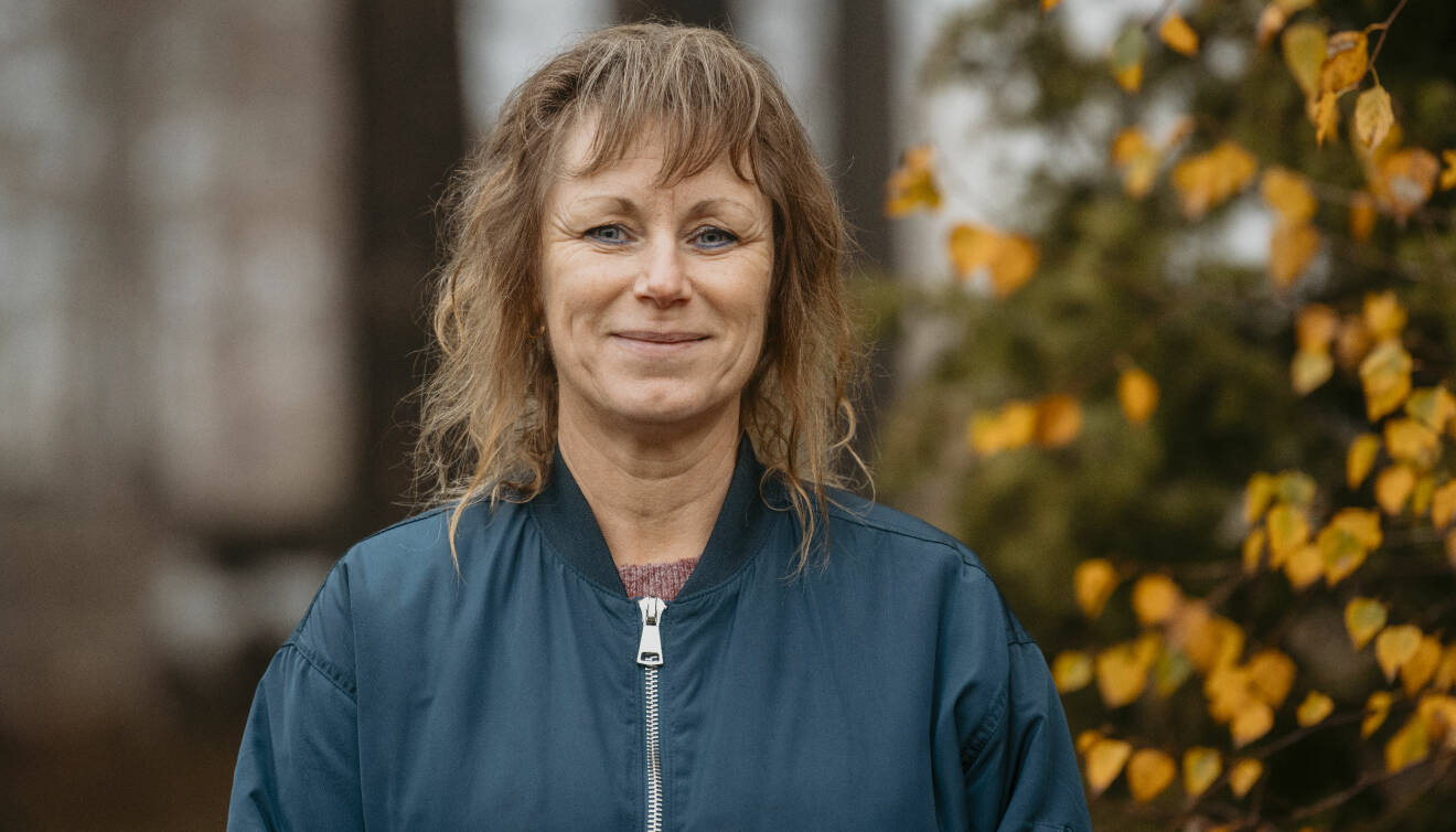 Porträttfotografi av Lena Aftelöv ute på gården framför ett träd med gula löv.