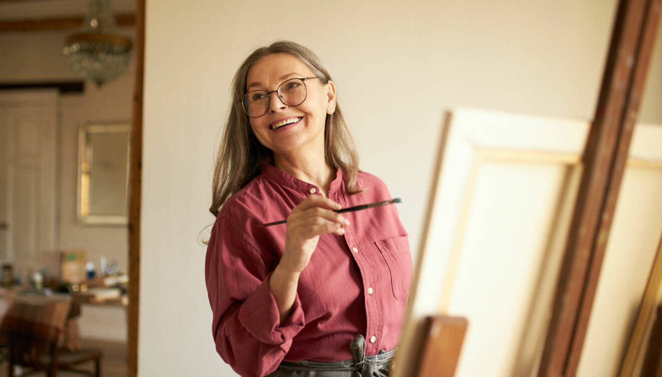 Glad kvinna i mogen ålder målar tavla.