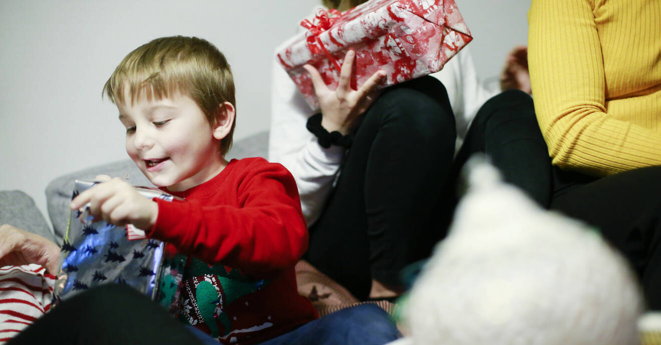 Julklappsöppning pågår och Edvin ler när han öppnar sin klapp som är inslagen i silverfärgat julklappspapper med svarta granar på.