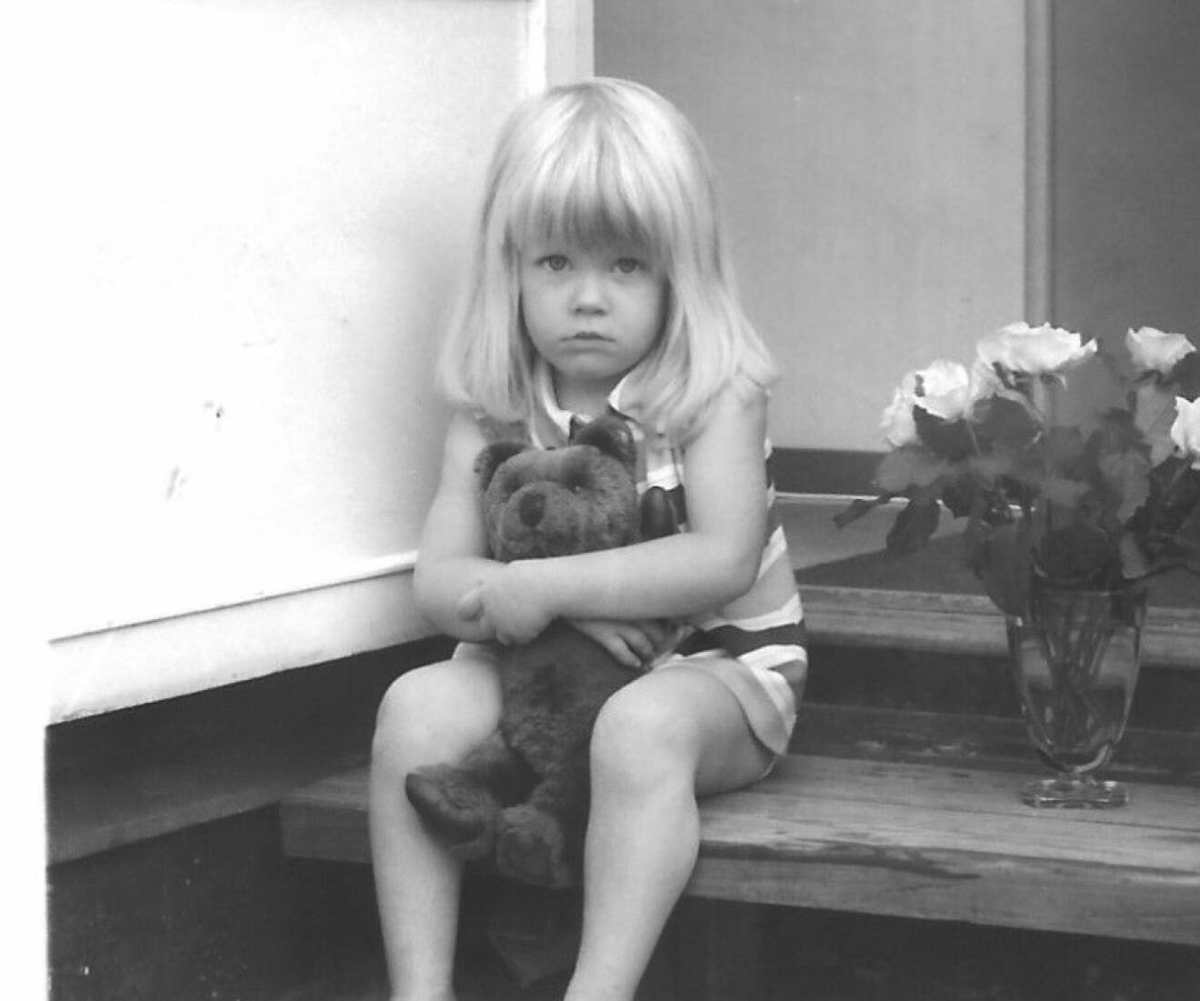 Anna Kansell som barn, sittande på en trappa med sin nalle i famnen.