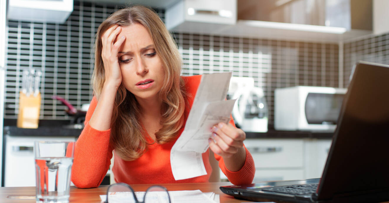 Ung kvinna sitter vid köksbordet för att betala sina räkningar och blir bekymrad över sin vardagsekonomi.