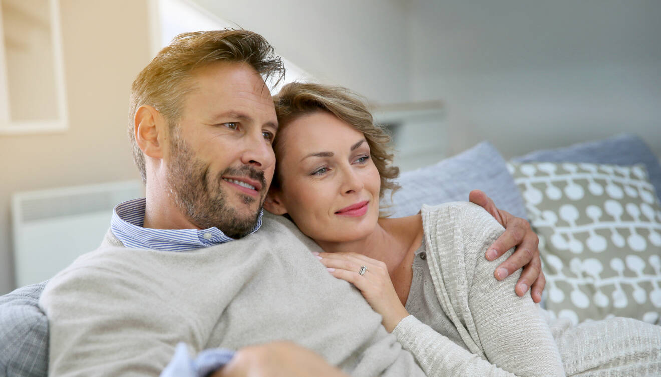Par i 35-40-årsåldern sitter tätt ihop i soffan och ser lyckliga ut.