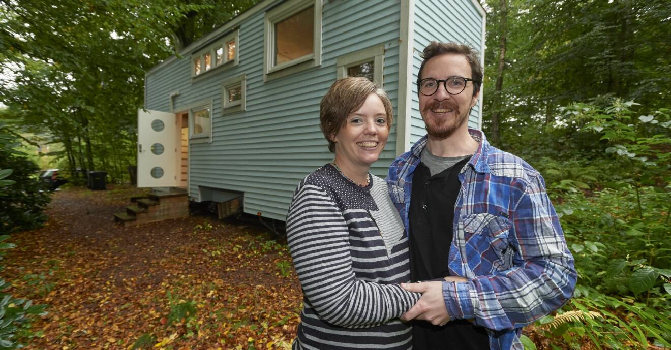 Marita och John står framför sitt tiny house på 16 kvadratmeter som ligger i en skogsdunge.