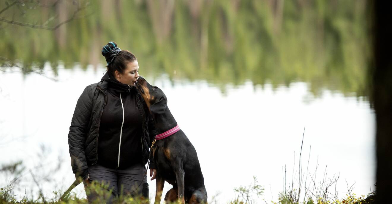 Unga änkan Emma får en puss av sin älskade dobermann-hund Dixie nere vid vattnet.