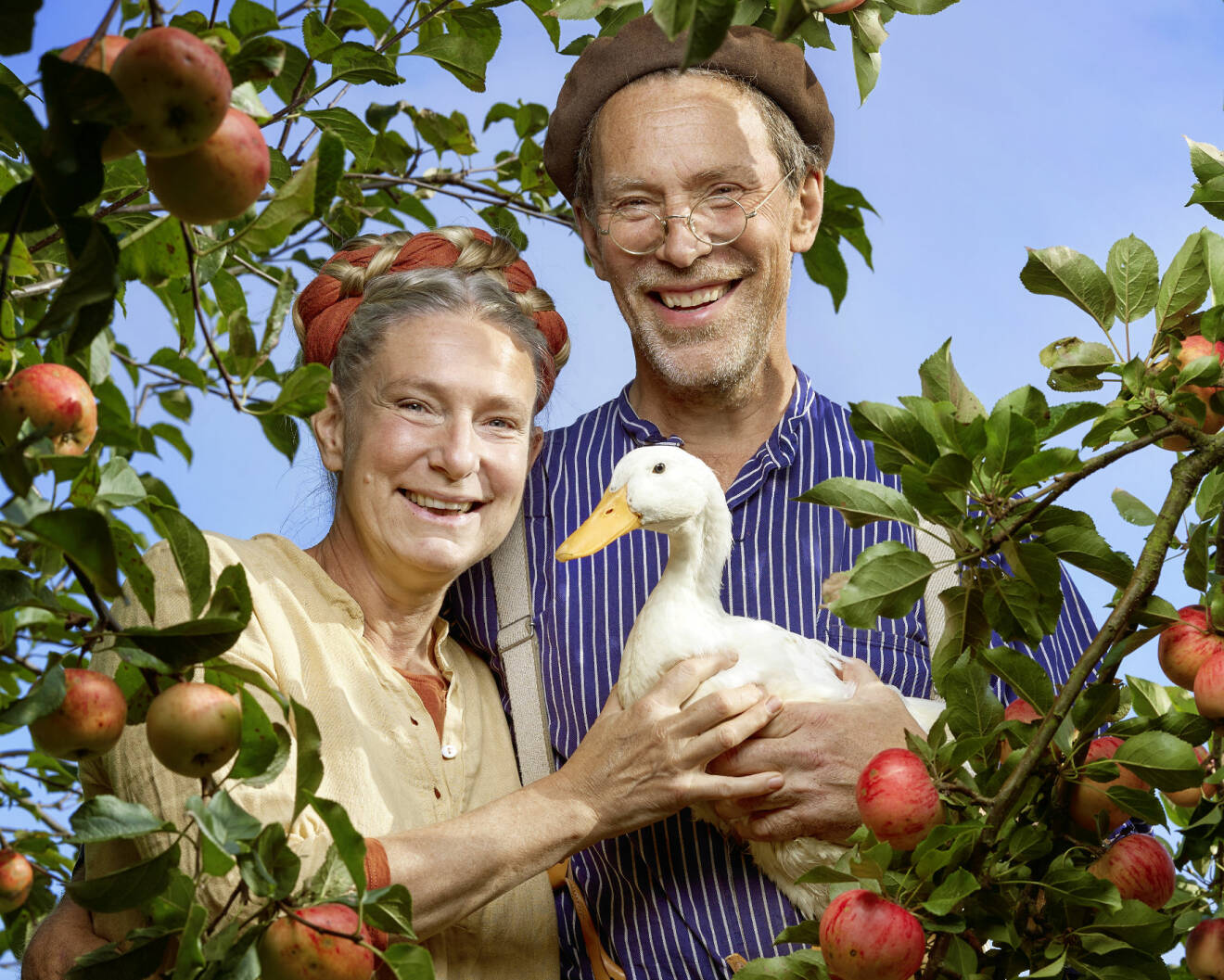 Pressbild från nya säsongen av Mandelmanns gård som har premiär i januari 2021. Marie och Gustav Mandelmann bland äppelträden tillsammans med en anka.