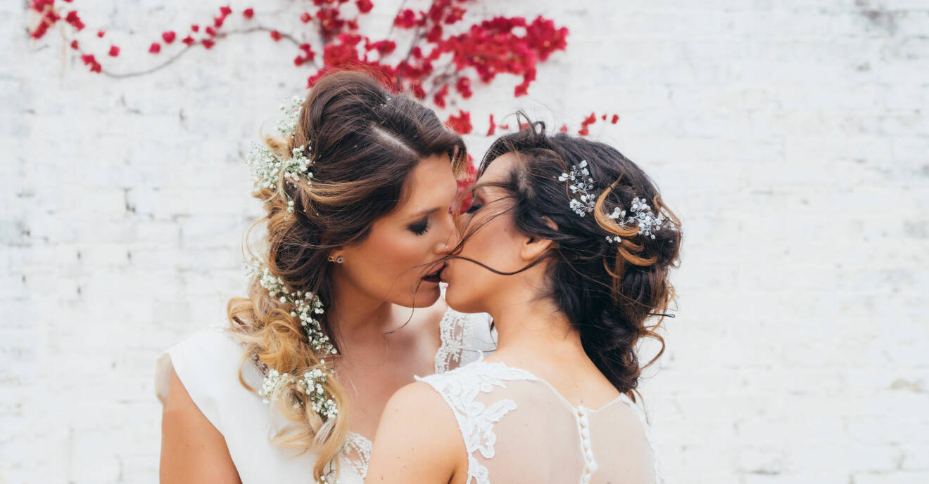 Två nygifta kvinnor i brudklänningar kysser varandra.
