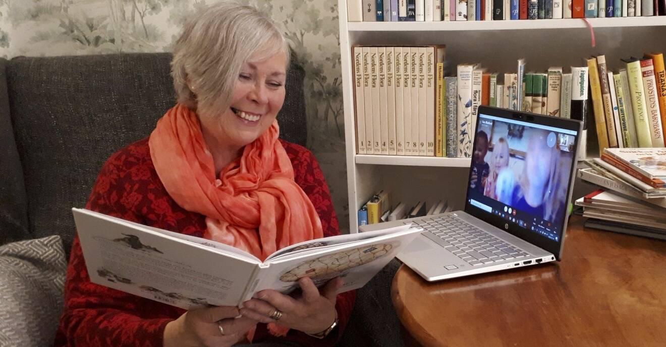 Karin sitter hemma vid ett bord läser sagor via Skype för sina barnbarn som bor någon annanstans.