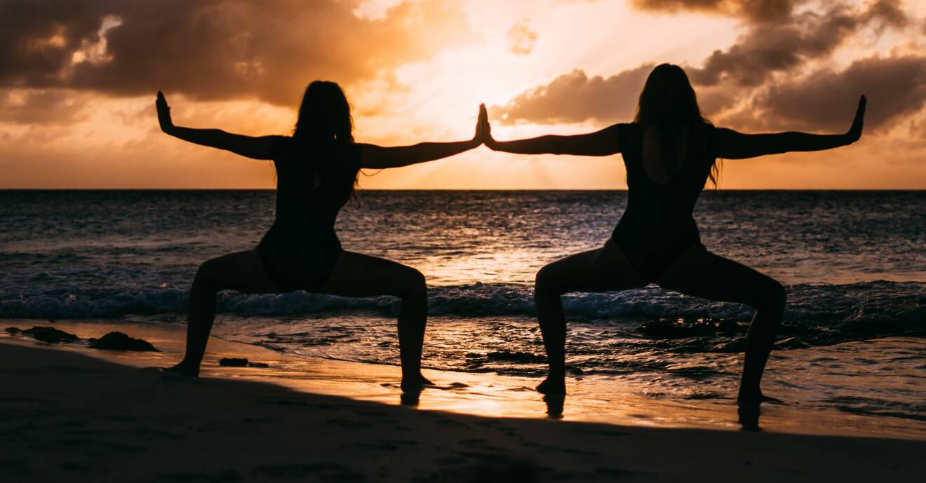 Två kvinnor som gör yoga på en strand och mår bättre av det på många olika sätt.