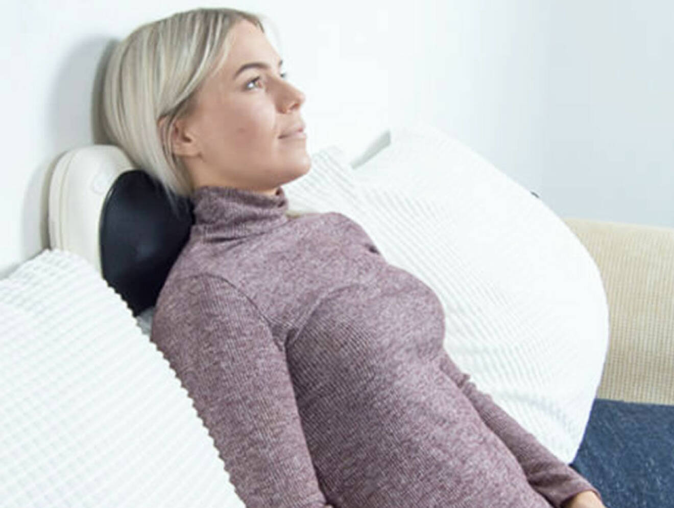Kvinna får massage av massagekudde i soffan.