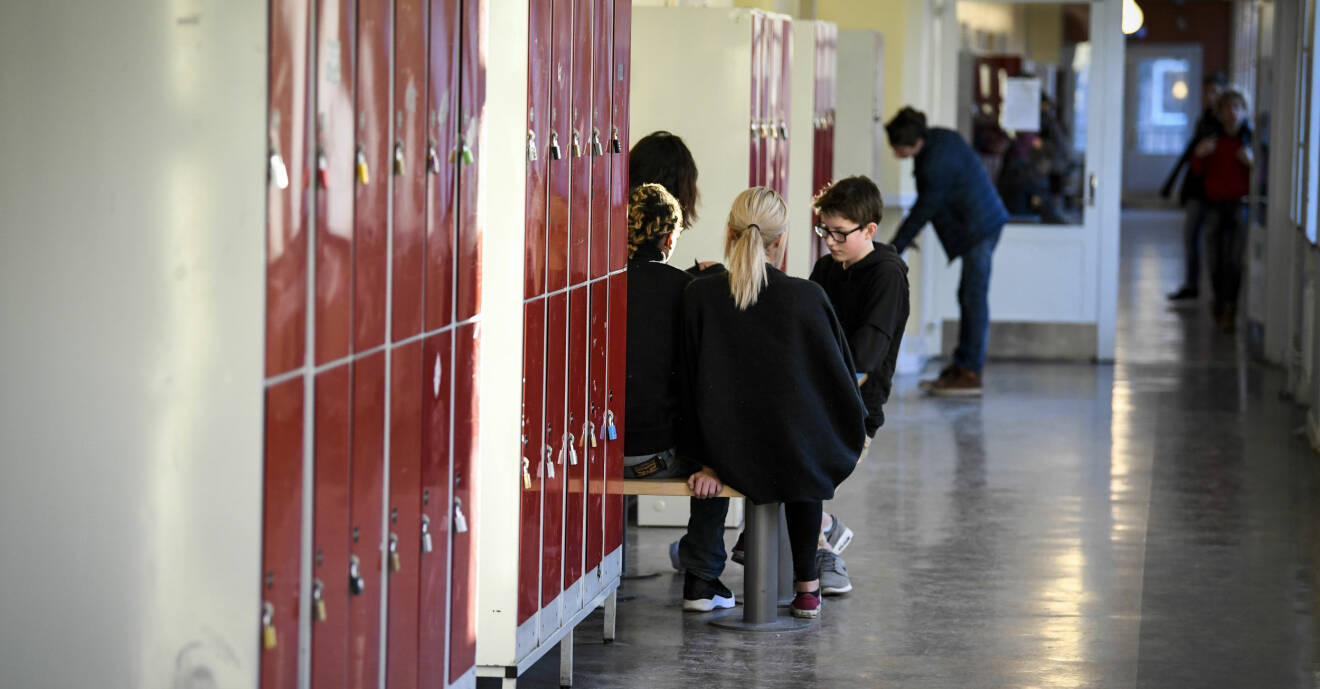 Elever hänger i skolkorridor med röda skåp.