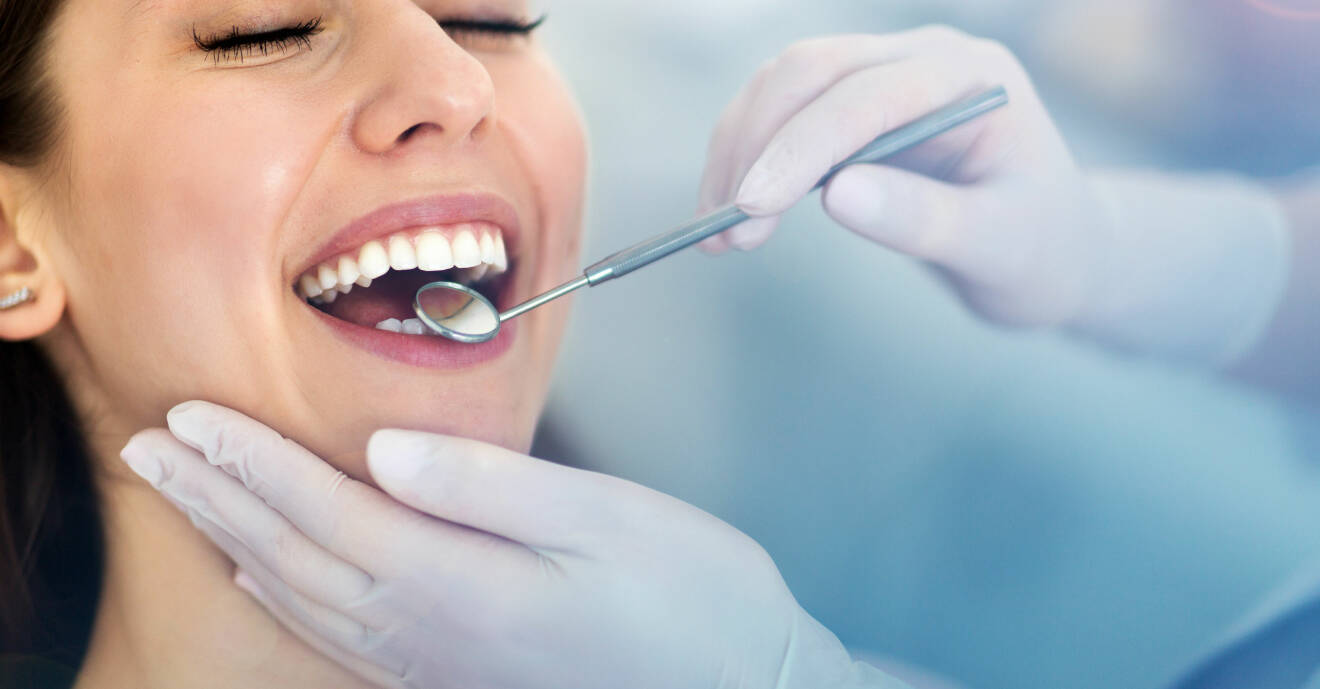 En kvinna är hos tandläkaren som kontrollerar hennes tänder för plack och tandsten med en spegel.
