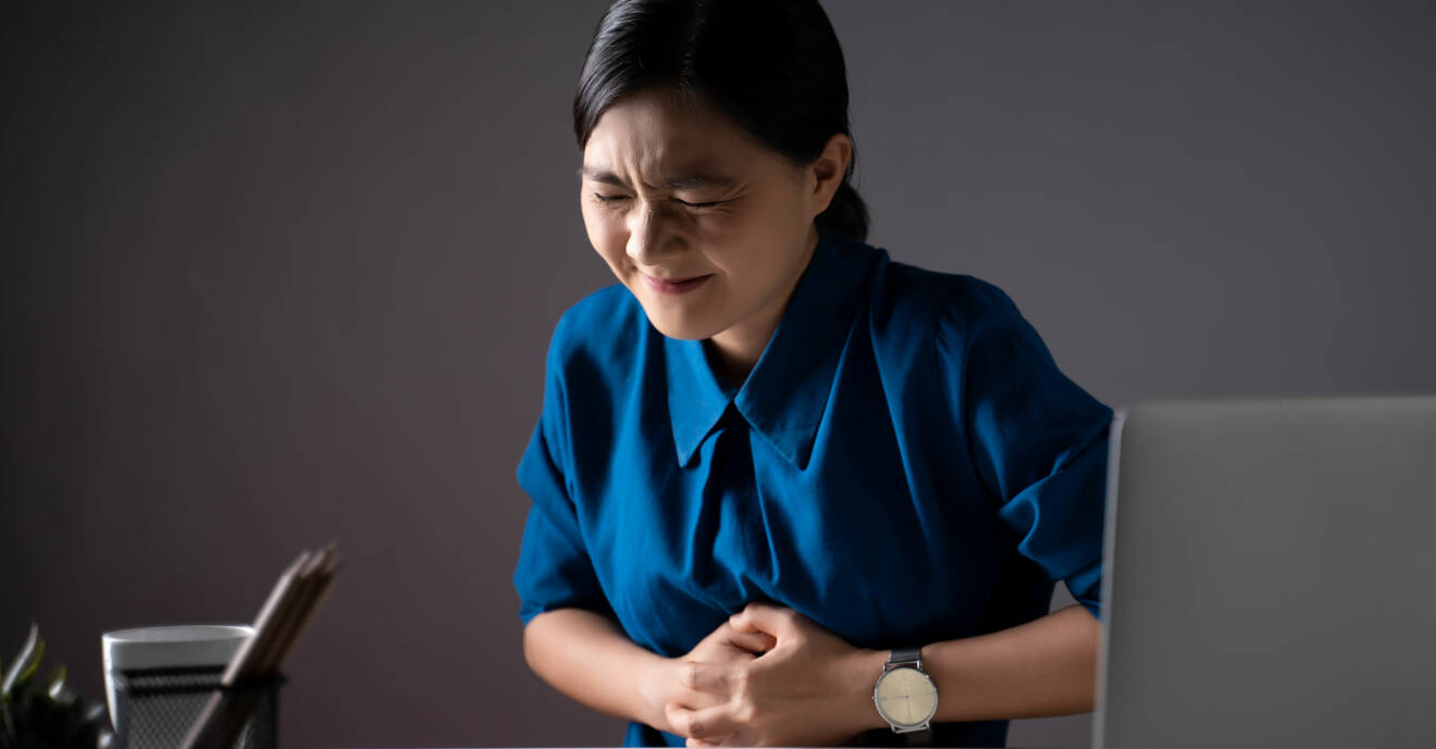 En kvinna som har fått ont i magen – ett symtom som kan tyda på magsår.