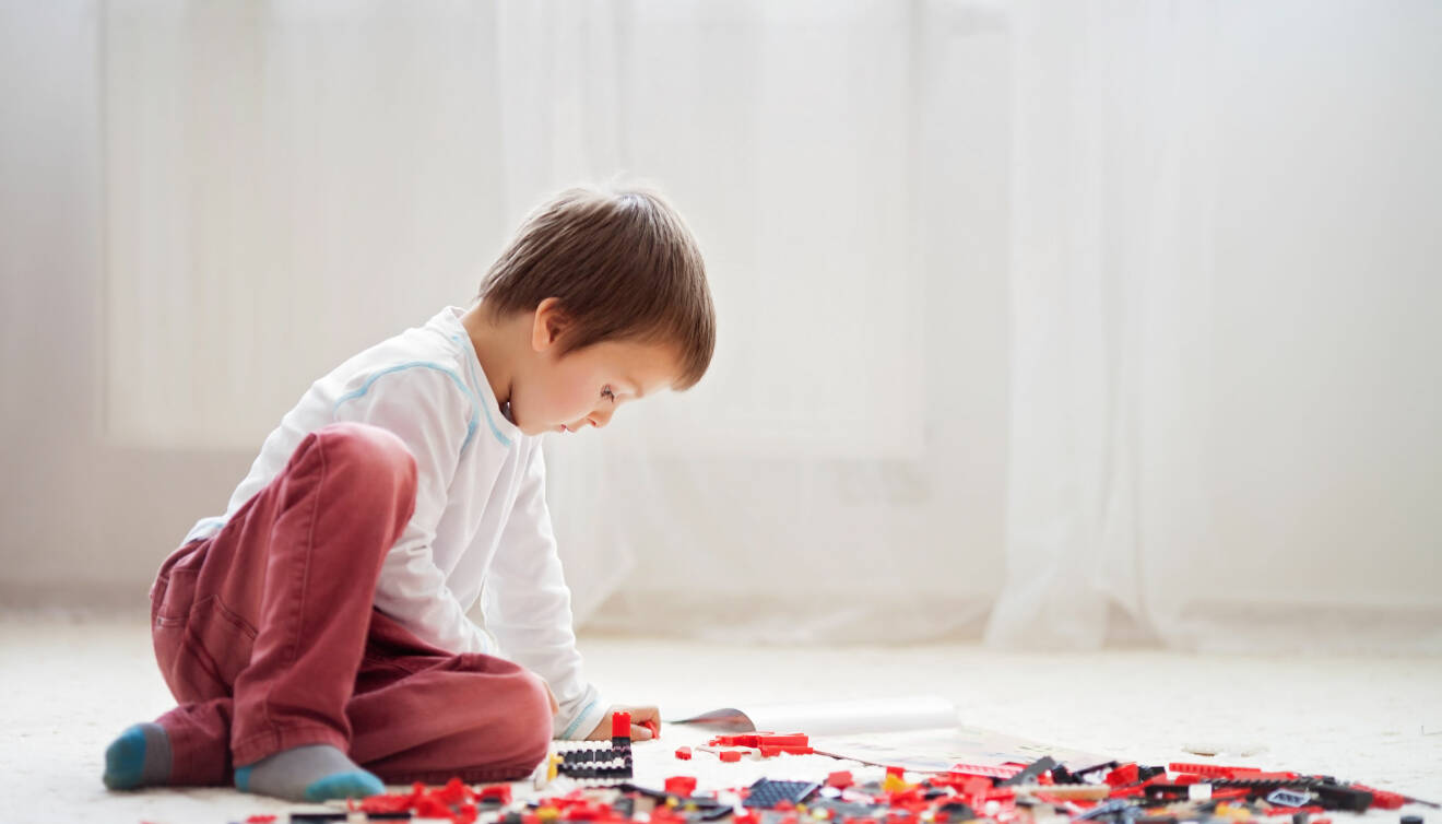 Liten pojke som troligtvis har autistiska drag sitter på golvet och leker koncentrerat med lego.