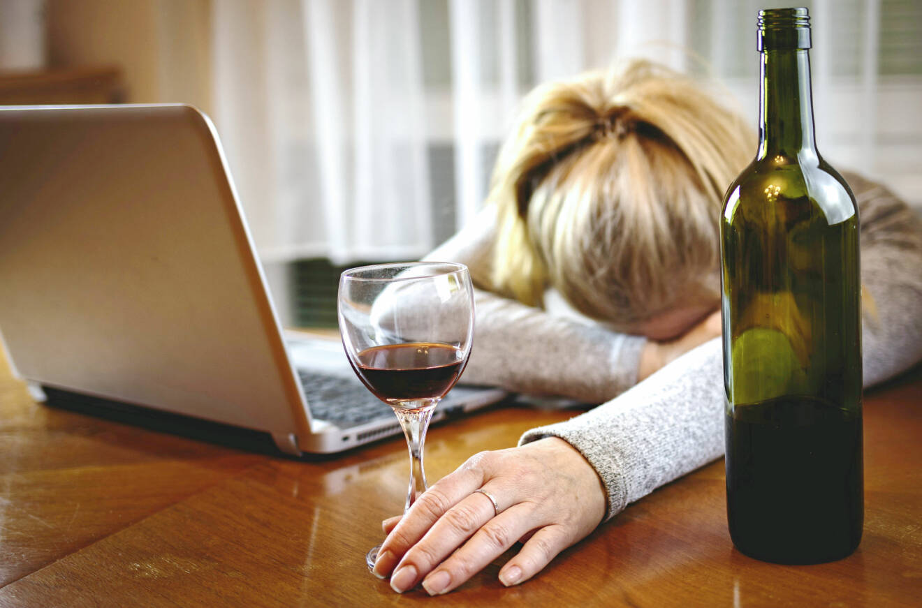 Kvinna utslagen framför datorn med vinglas och en flaska vin.