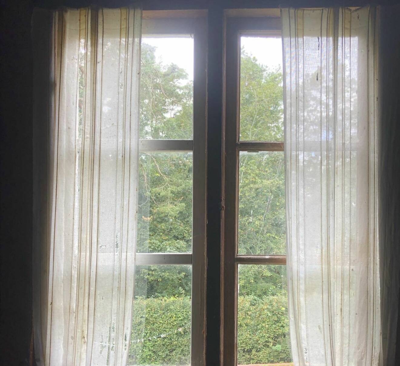 I ett fönster till ett övergivet hus hänger trasiga, solblekta gardiner.