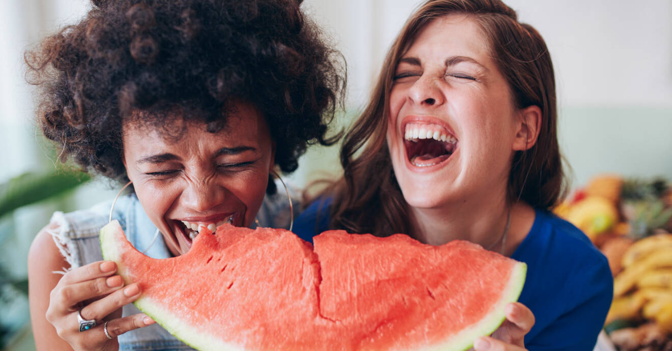 Två kvinnor skrattar medan de äter vattenmelon