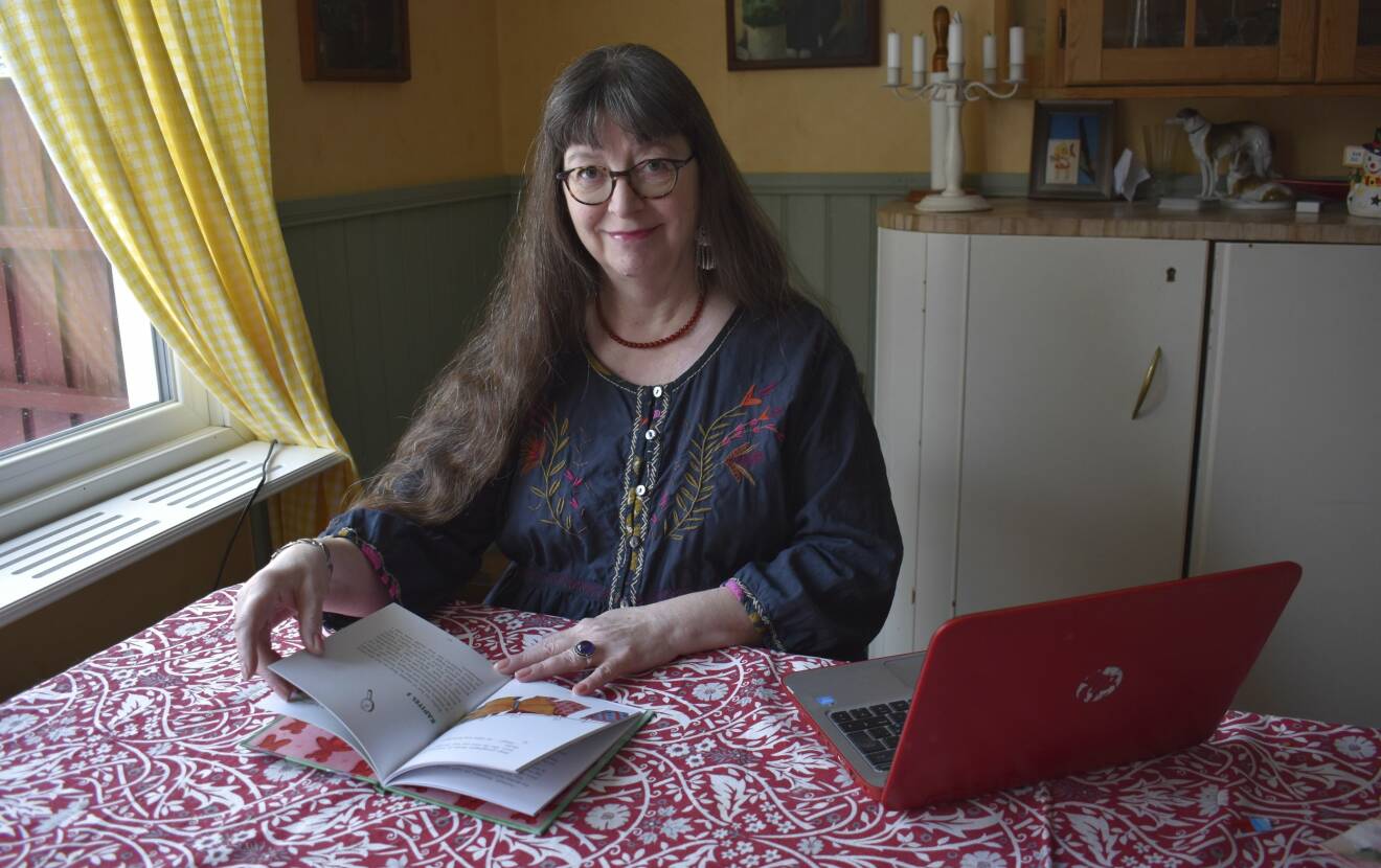 Irene Svensson bläddrar i sin färdiga bok, där hon sitter med sin laptop vid köksbordet.
