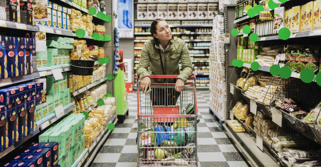 Kvinna lutar sig mot en kundvagn i en matvaruaffär.
