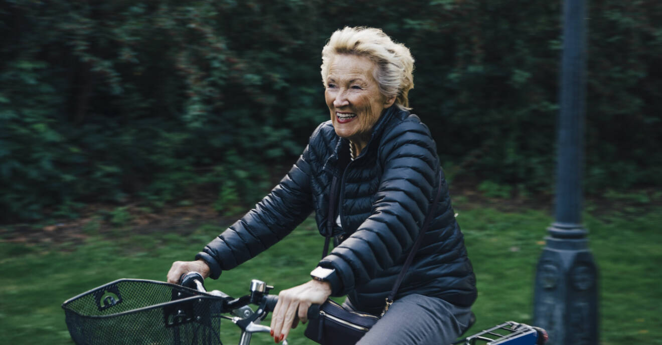 Leende äldre kvinna cyklar cykelväg