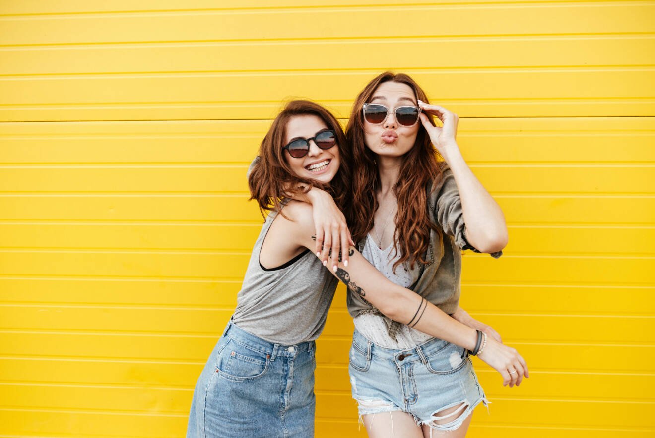Två vänner med solglasögon och gul vägg
