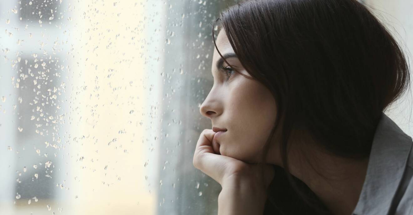 Ledsen ung kvinna tittar ut genom ett fönster