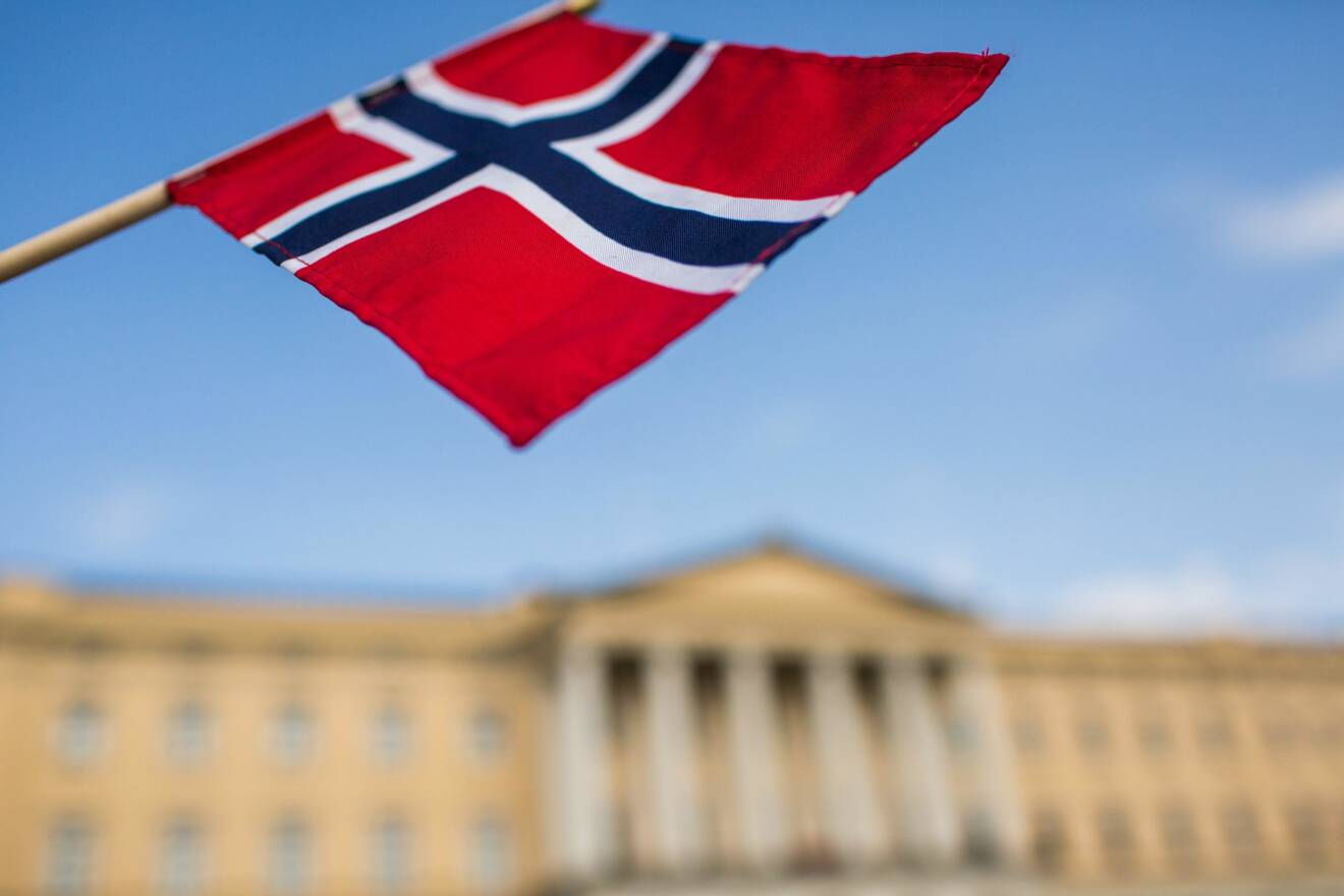 Norges flagga vajar i vinden mot en klarblå himmel.