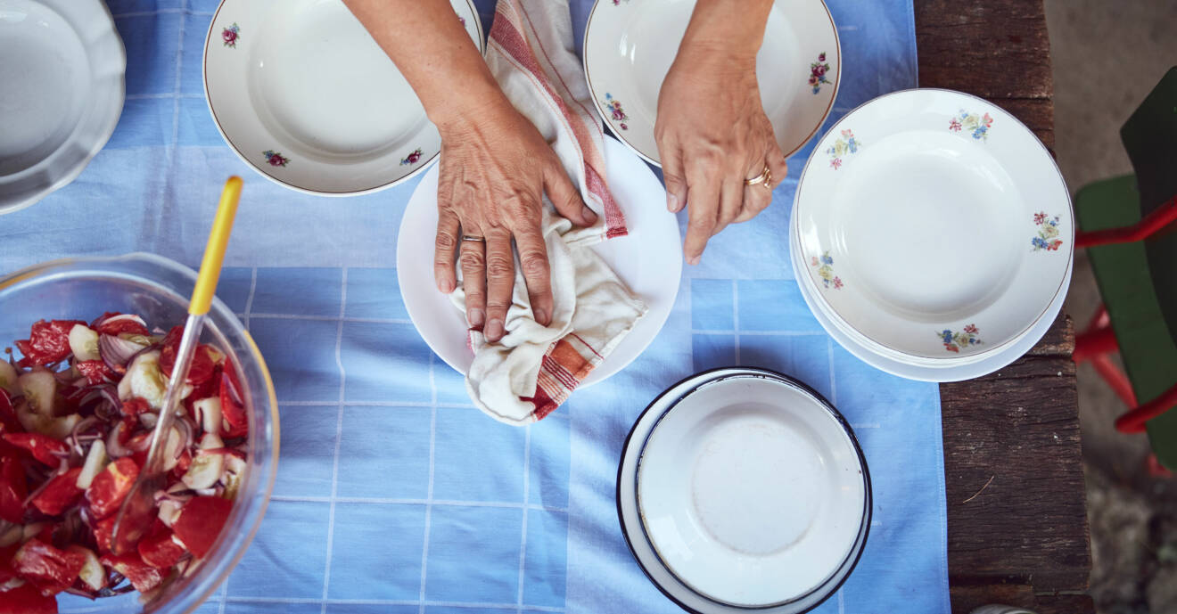 En kvinna torkar av porslin på ett bord.