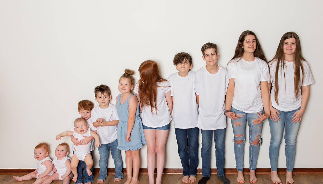 De elva barnen står uppradade, de minsta till vänster och de längsta till höger, alla är klädda i vitt och ljusblått.