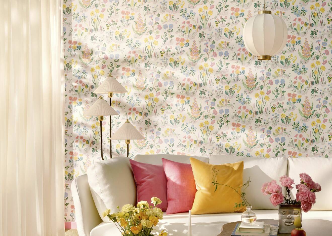 Ljus atpet med mönster i pastellfärger, vit soffa med två rosa kuddar och en gul.