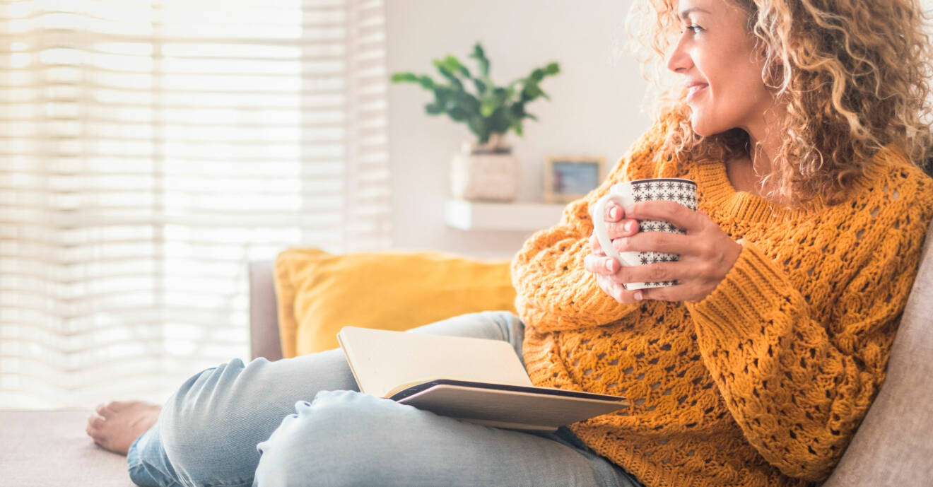 Kvinna läser och njuter av en kopp te och dagsljuset.