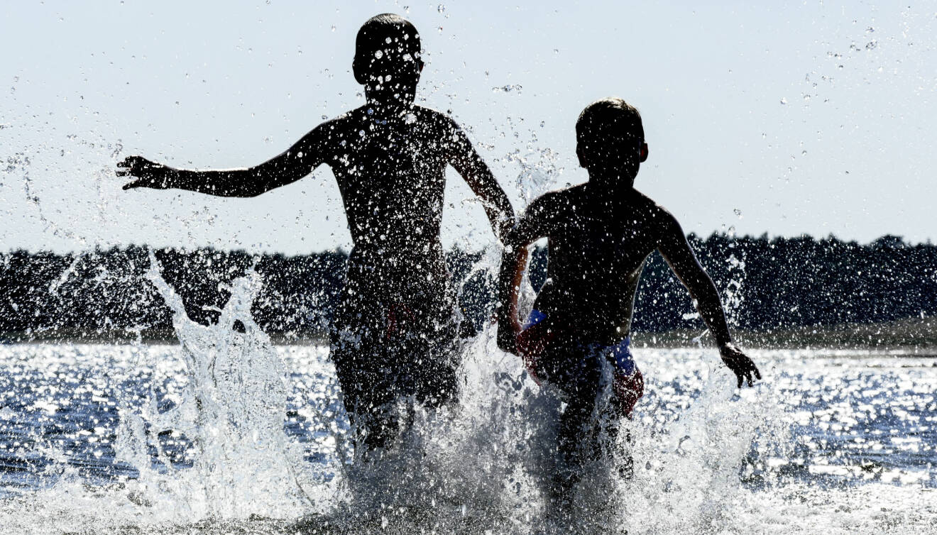Två pojkar som springer i vattnet som stänker en solig dag.
