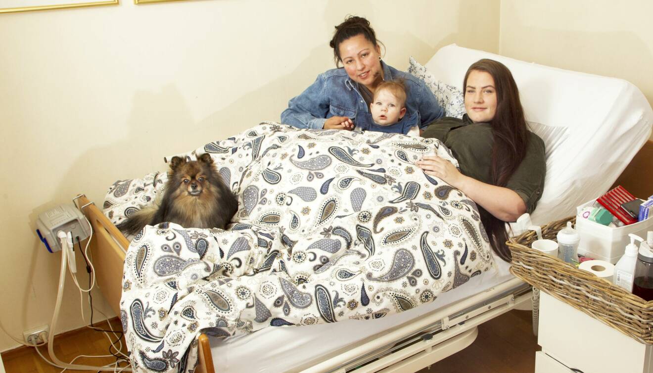 Två kvinnor, deras dotter och en hund i en sjuksäng.