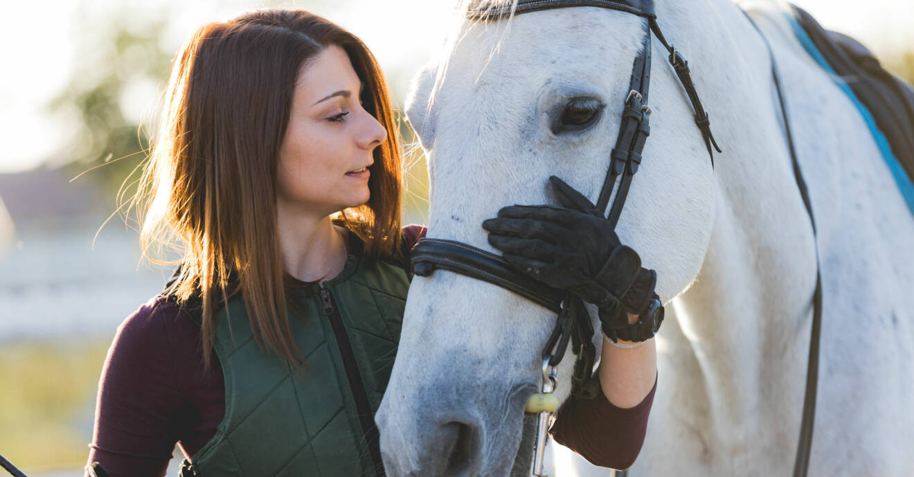 Ung kvinna håller armen runt sin hästs mule och tittar den i ögonen.
