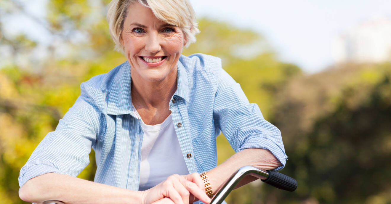 Mogen kvinna lutar sig över cykelstyret med ett leende.